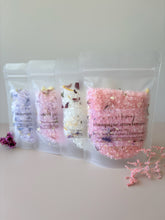 Assorted bath soak pouches in pastel colours, including black raspberry and vanilla, sweet pea and jasmine, Miss Dior and champagne strawberries, displayed in a row.