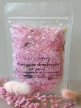Champagne strawberries bath soak in a clear resealable pouch with pastel pink crystals and dried floral botanicals
